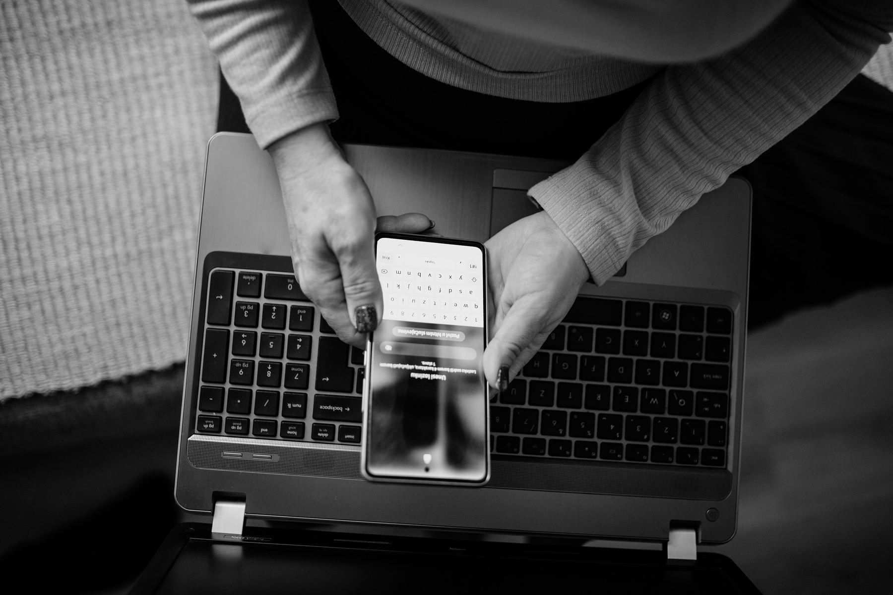 Hands holding a phone over a laptop's keyboard, an app open on its screen