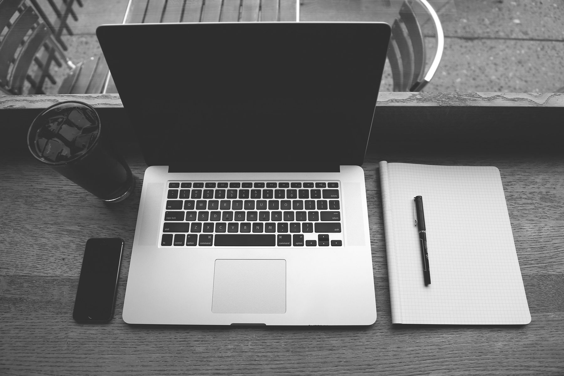 An open laptop on a wooden table, with a phone, a notebook and a pen beside it