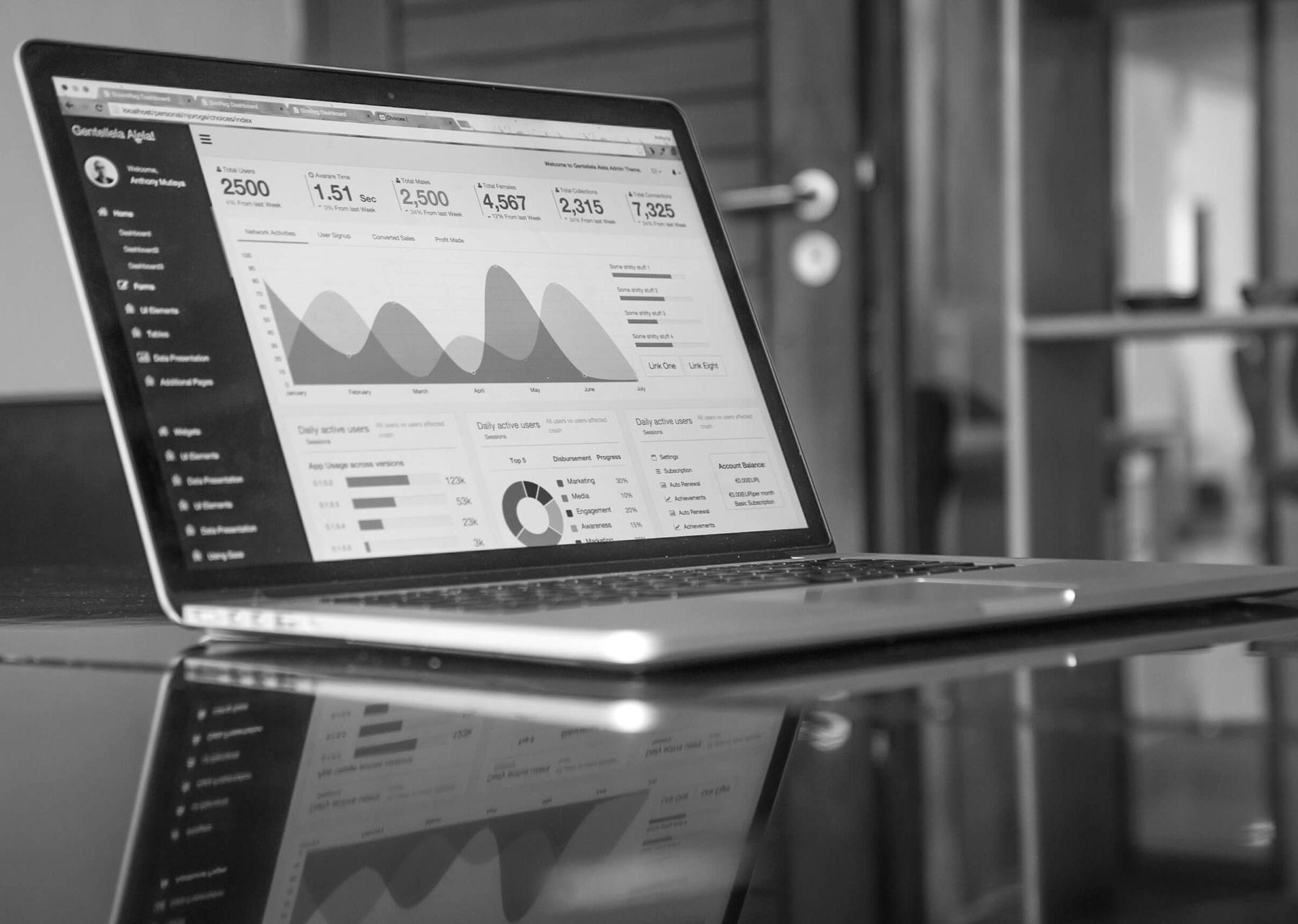 A laptop on a glossy table, a dashboard of figures and charts on its screen