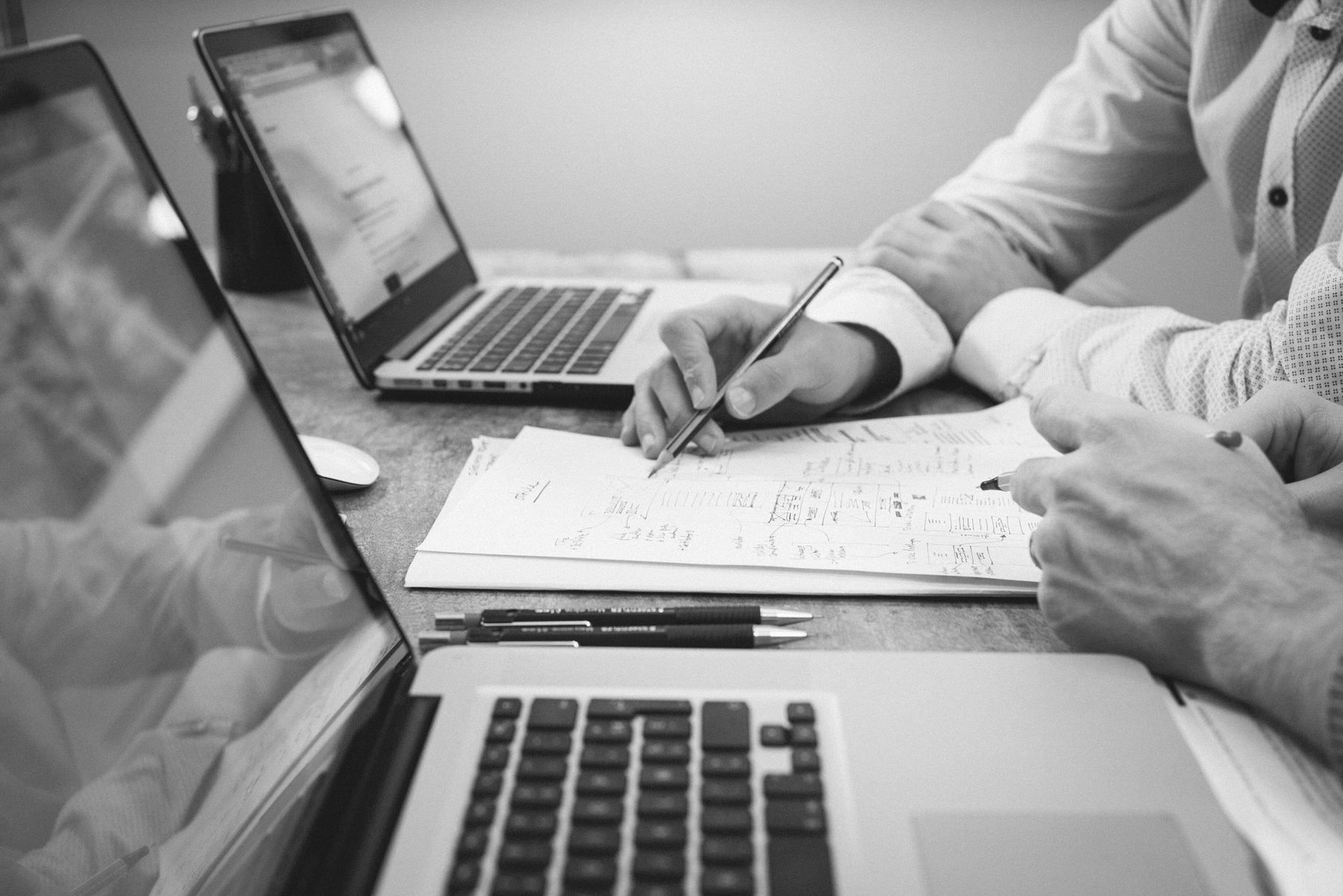 Two people working together at one table, with two laptops and a sheet of notes