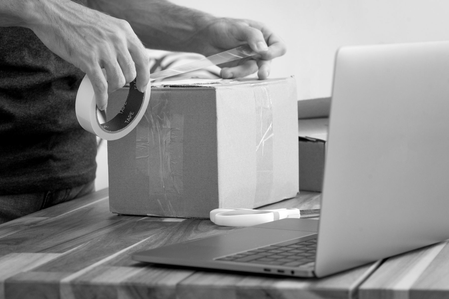 Hands sealing an order box with tape beside a laptop